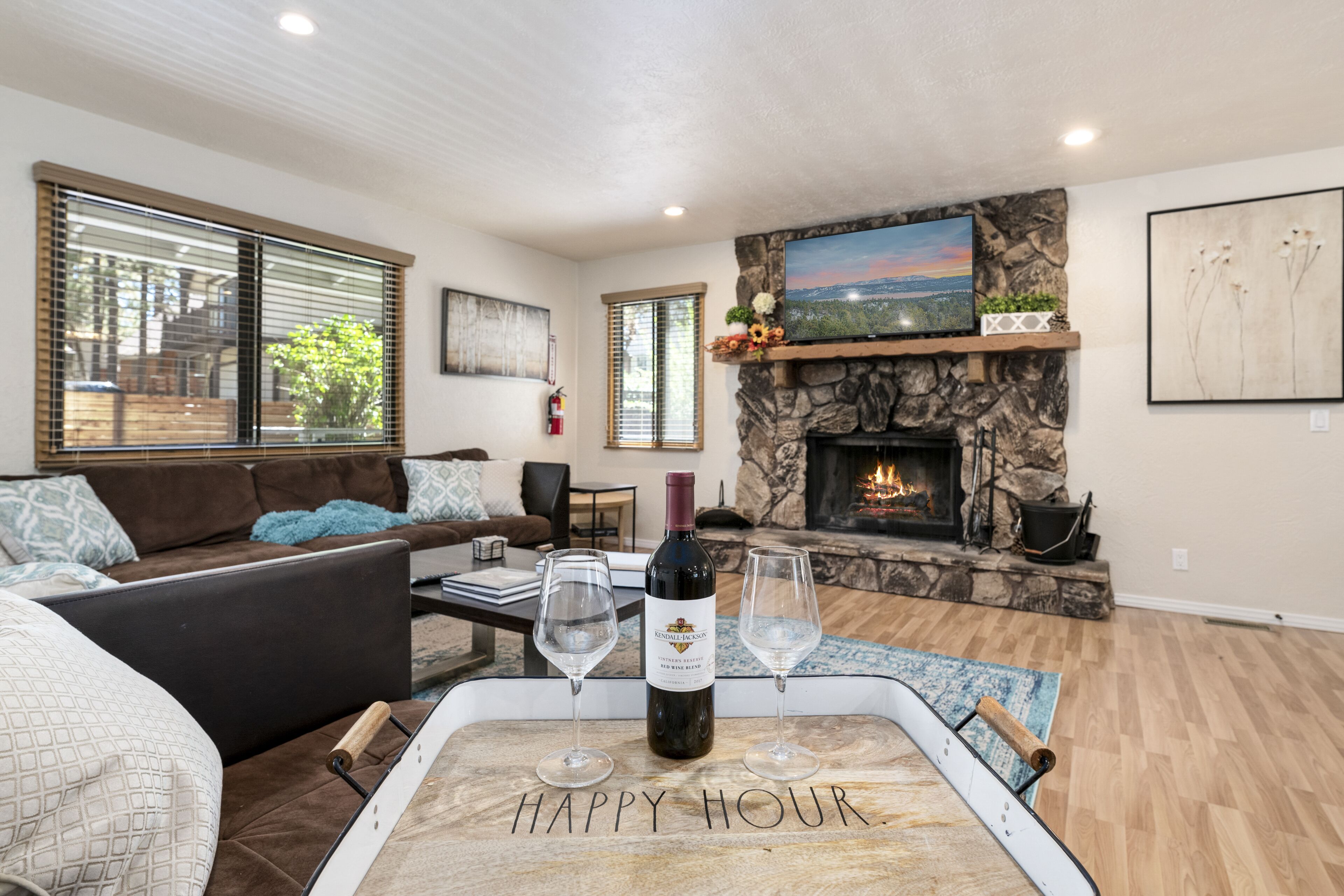 A cozy living room with a stone fireplace, a sofa, and a tray with a bottle of wine and glasses.
