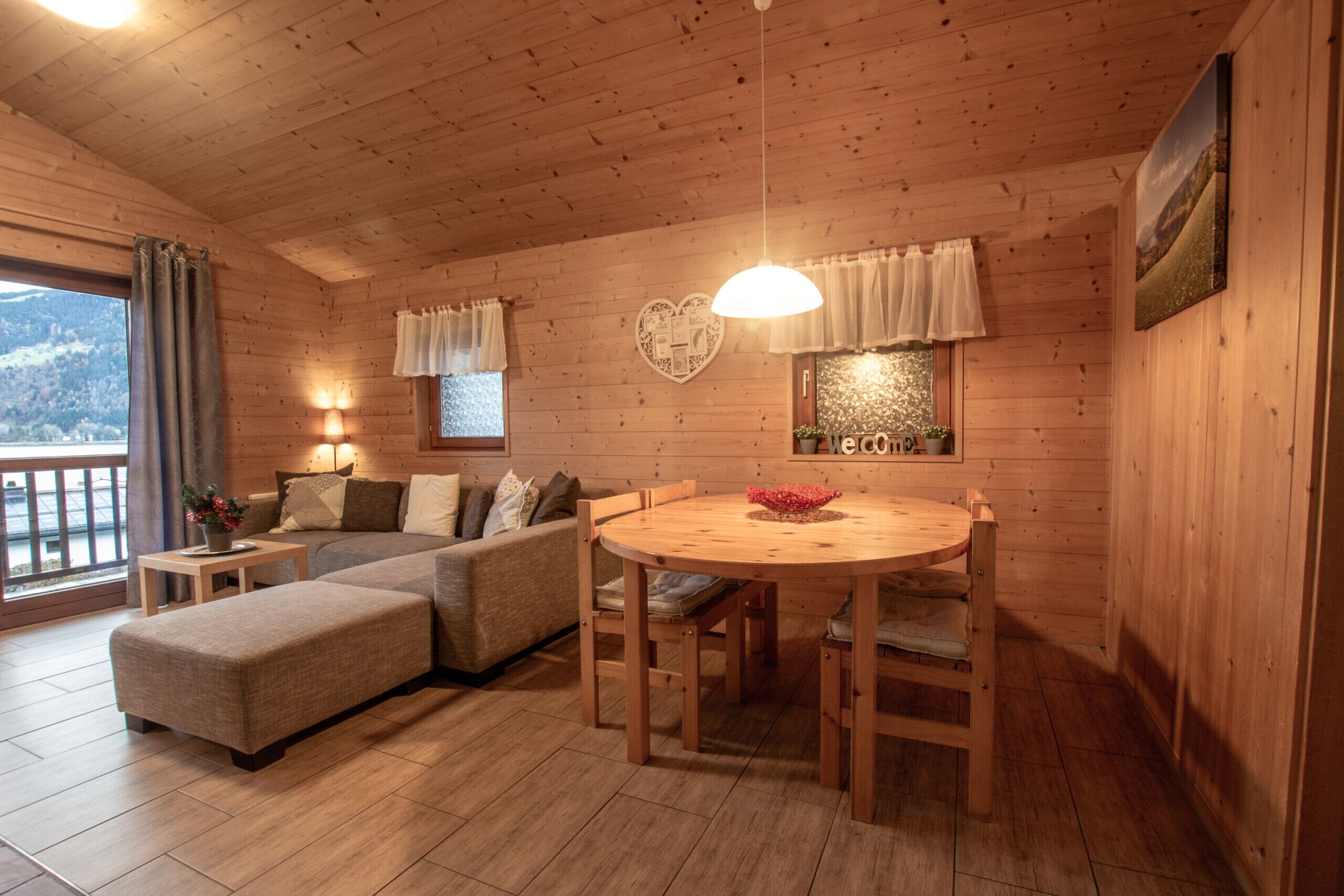 A cozy wooden cabin interior with a round wooden table, a sofa, and a dining area.