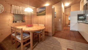 A wooden interior with a round dining table, chairs, a hanging light fixture, a welcome sign, a window with a view of a field, and a kitchen area. - Lake and Mountain View (Zell am See)
