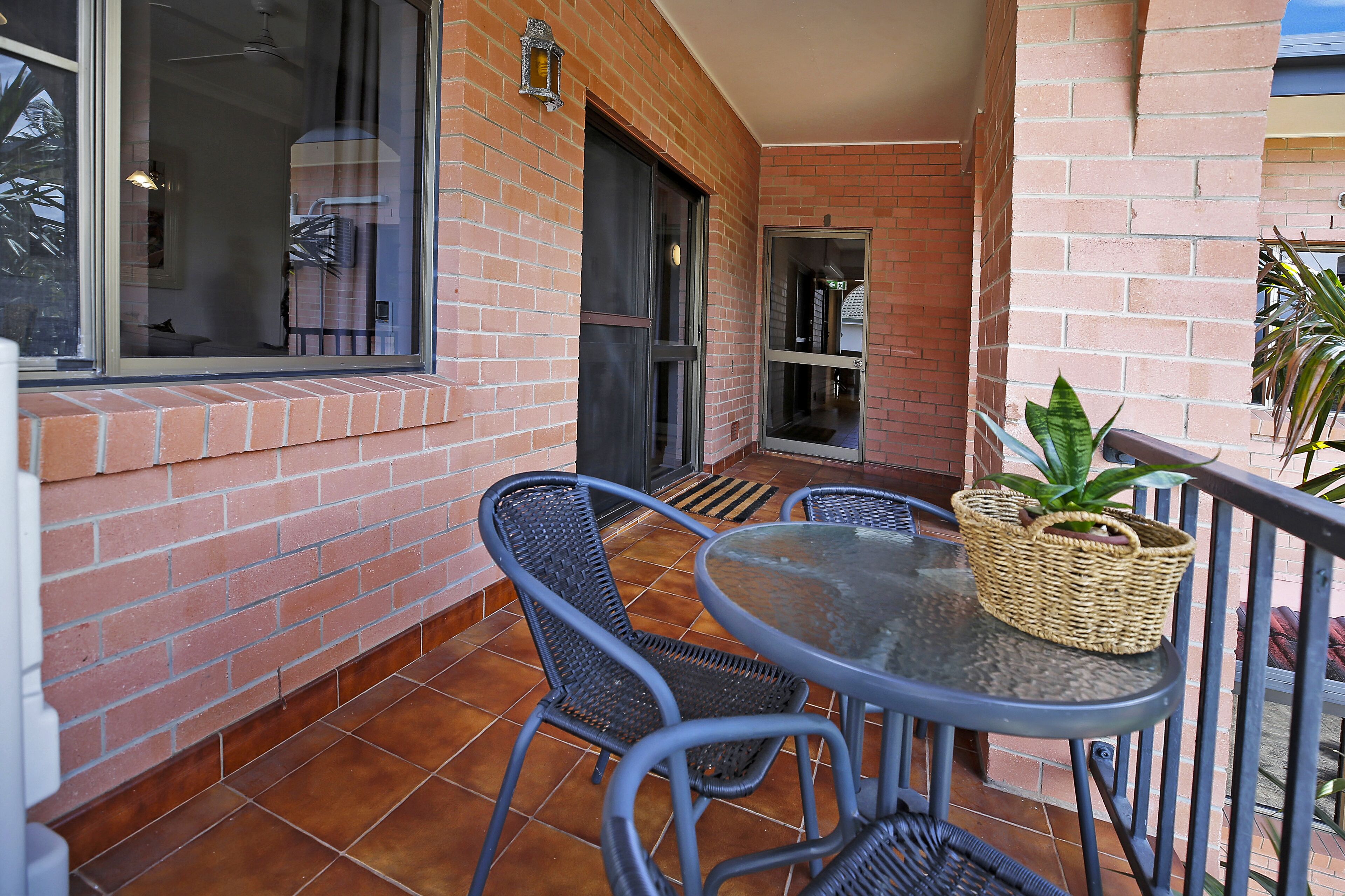 A patio with a round table and two chairs, a wicker basket on the table, and a potted plant.