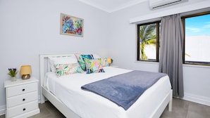 A neatly arranged bedroom with a bed, a bedside table, a lamp, and a window with curtains. - On the Esplanade (Cairns North)