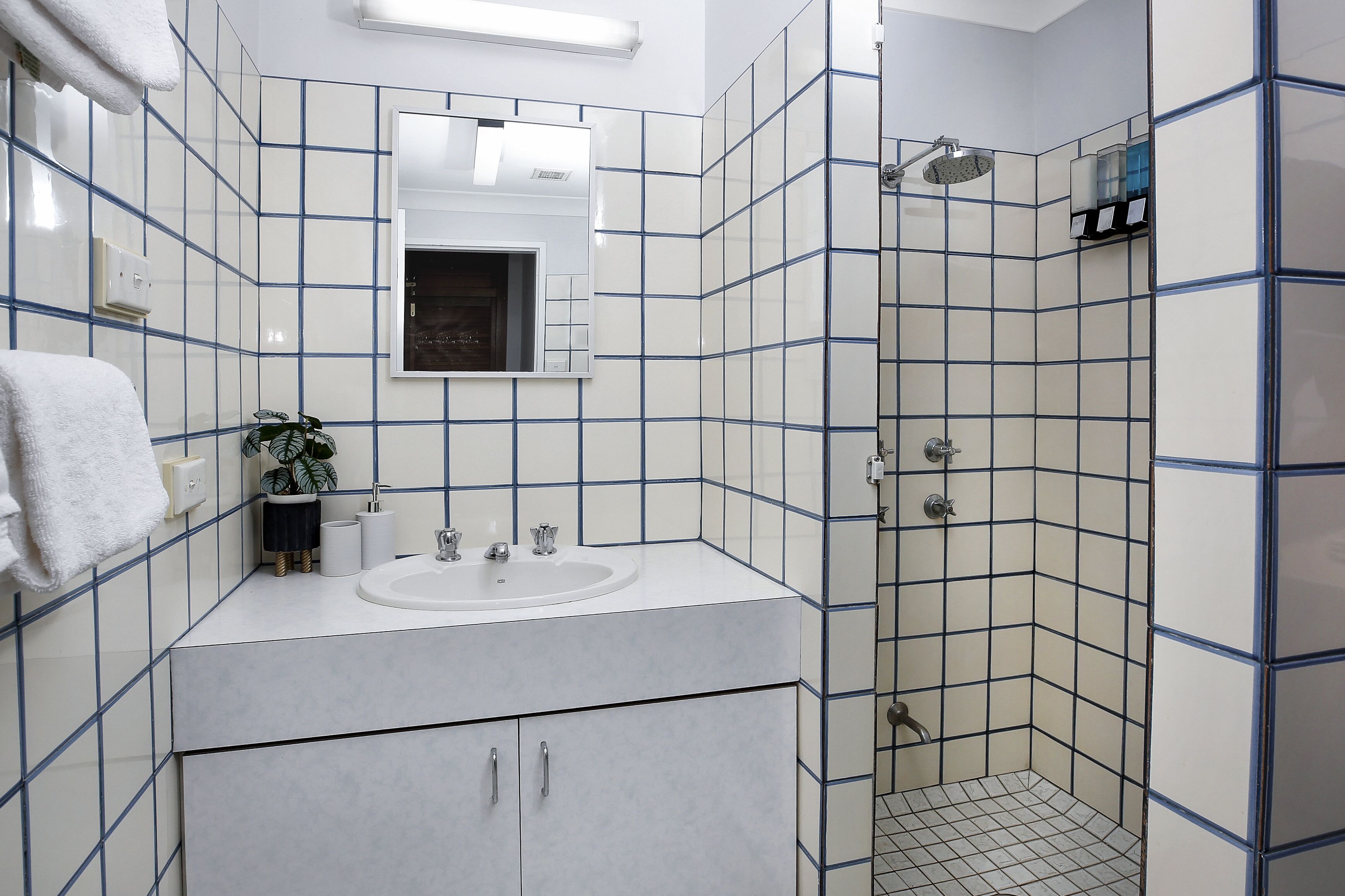 A bathroom with white tiles, a sink, a mirror, and a shower.