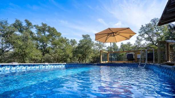 A clear blue swimming pool with a wooden deck and an umbrella.