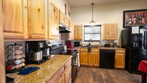 A kitchen with wooden cabinets, a granite countertop, a stainless steel range, a black refrigerator, and a window with blinds.