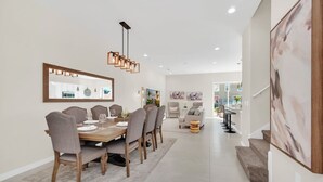 A modern dining area with a wooden table and chairs, a hanging light fixture, and a large abstract painting on the wall.