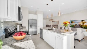 A modern kitchen with granite countertops, a stainless steel refrigerator, and a large island with a sink.