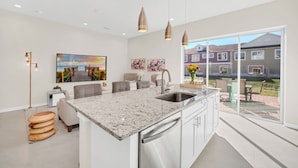 A modern kitchen with a granite countertop, stainless steel sink, and a large window offering a view of a residential area.