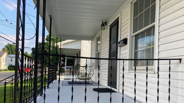 A covered porch with a black railing, a door, and a window.