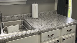 A kitchen with white cabinets, a granite countertop, a stainless steel sink, and a window with blinds.