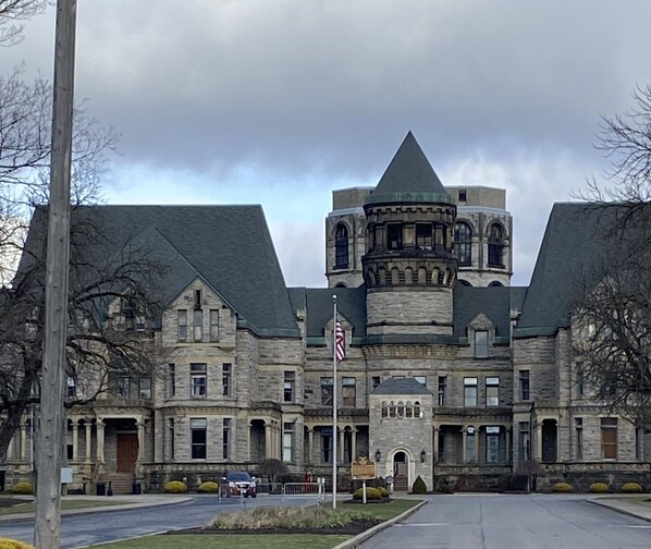 A large, historic stone building with a central turret and symmetrical wings, featuring a flagpole and a well-maintained lawn.