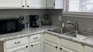 A kitchen with white cabinets, a granite countertop, a microwave, a coffee maker, and a sink.
