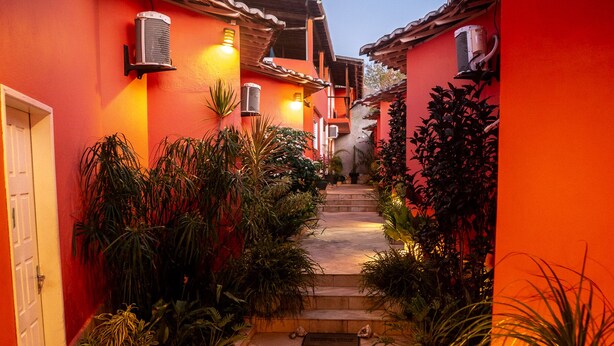 A narrow, brightly lit alleyway with steps leading to a door, surrounded by lush greenery and red walls. - Pousada Vento Terral (Tibau do Sul)