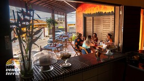 An outdoor dining area with tables and chairs, a view of the street, and a building with a distinctive facade. - Pousada Vento Terral (Tibau do Sul)