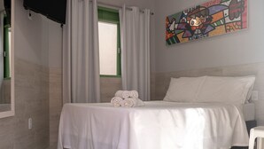 A bedroom with a bed, white curtains, a painting, and a TV mounted on the wall. - Pousada Vento Terral (Tibau do Sul)
