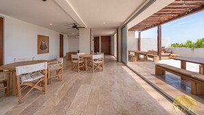 Un'ampia area interna con tavoli e panche in legno, ampie finestre e una ventola a soffitto.