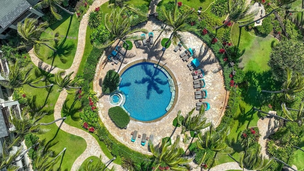 Una vista aerea di un resort con una piscina centrale circondata da lettini e palme.