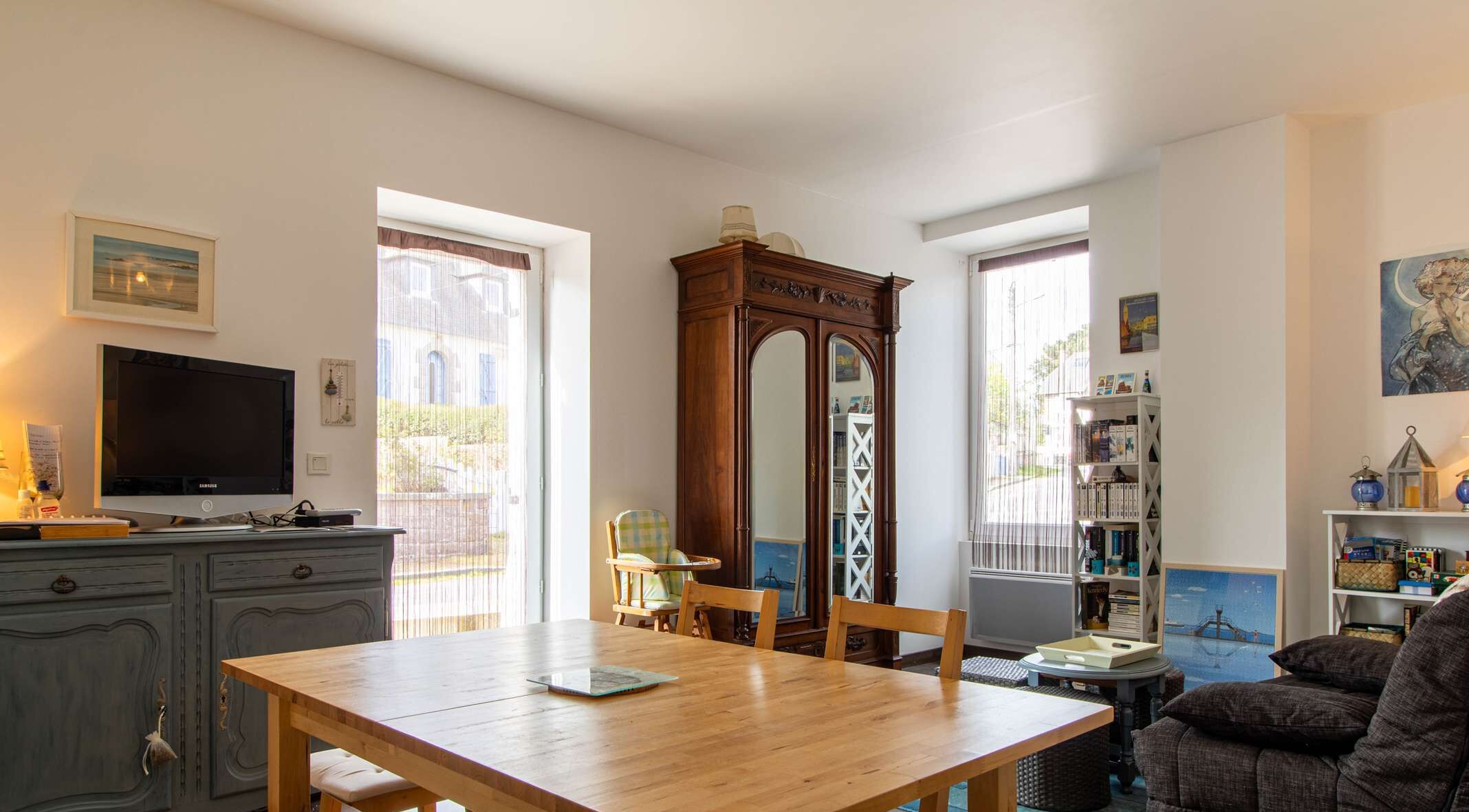 Ein Wohnzimmer mit einem Holztisch, einem Fernseher, einem Bücherregal und einem großen Spiegel.