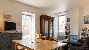 A living room with a wooden table, a television, a bookshelf, and a large mirror. - Apartment near beaches in Fréhel | 4 guests | Ref 359 (FREHEL)