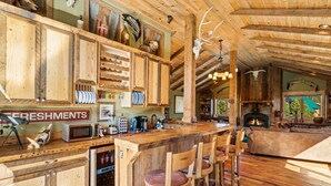 Interior rústico con taburetes de madera, zona de cocina y chimenea.