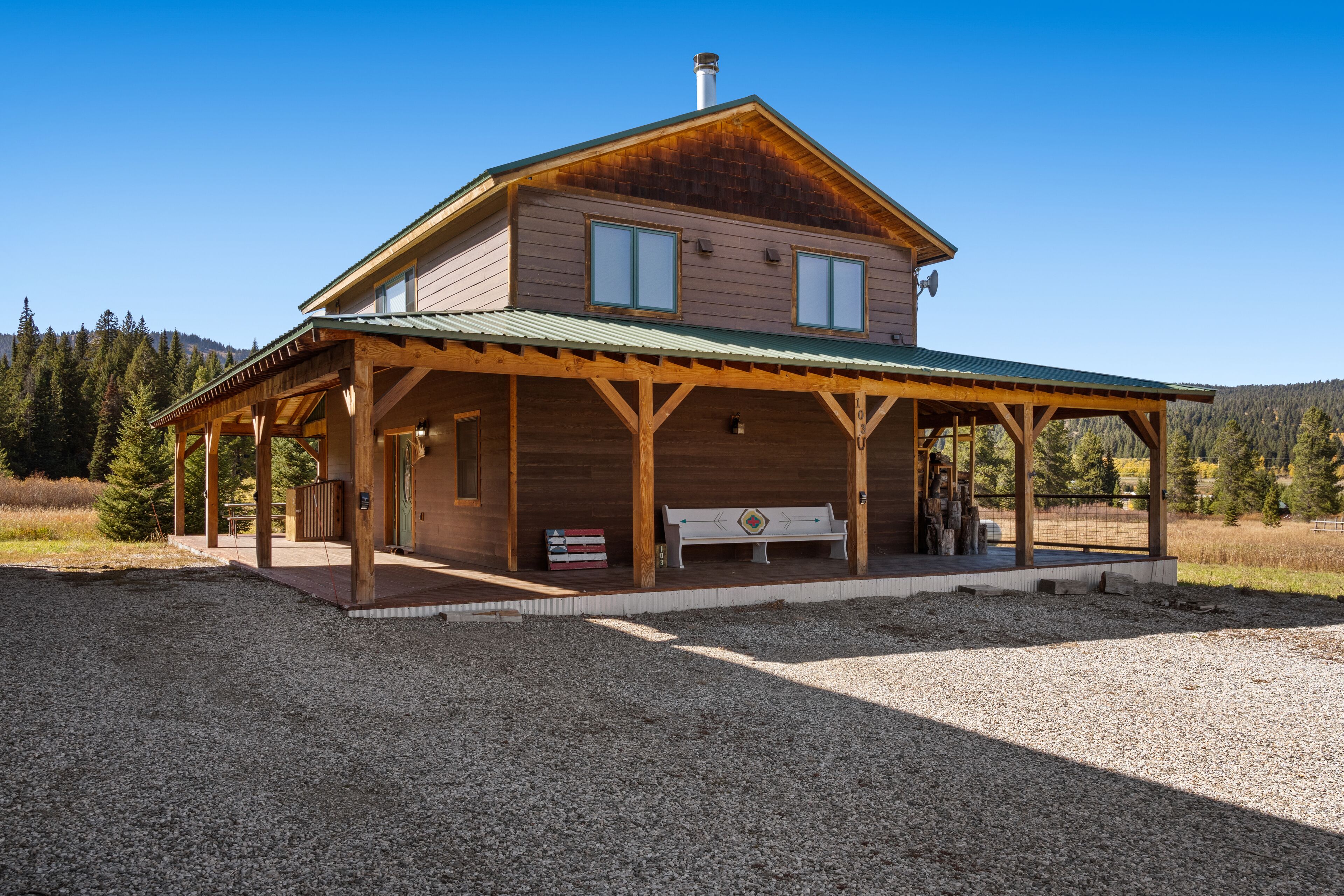 A two-story wooden cabin with a covered porch and a gravel driveway.