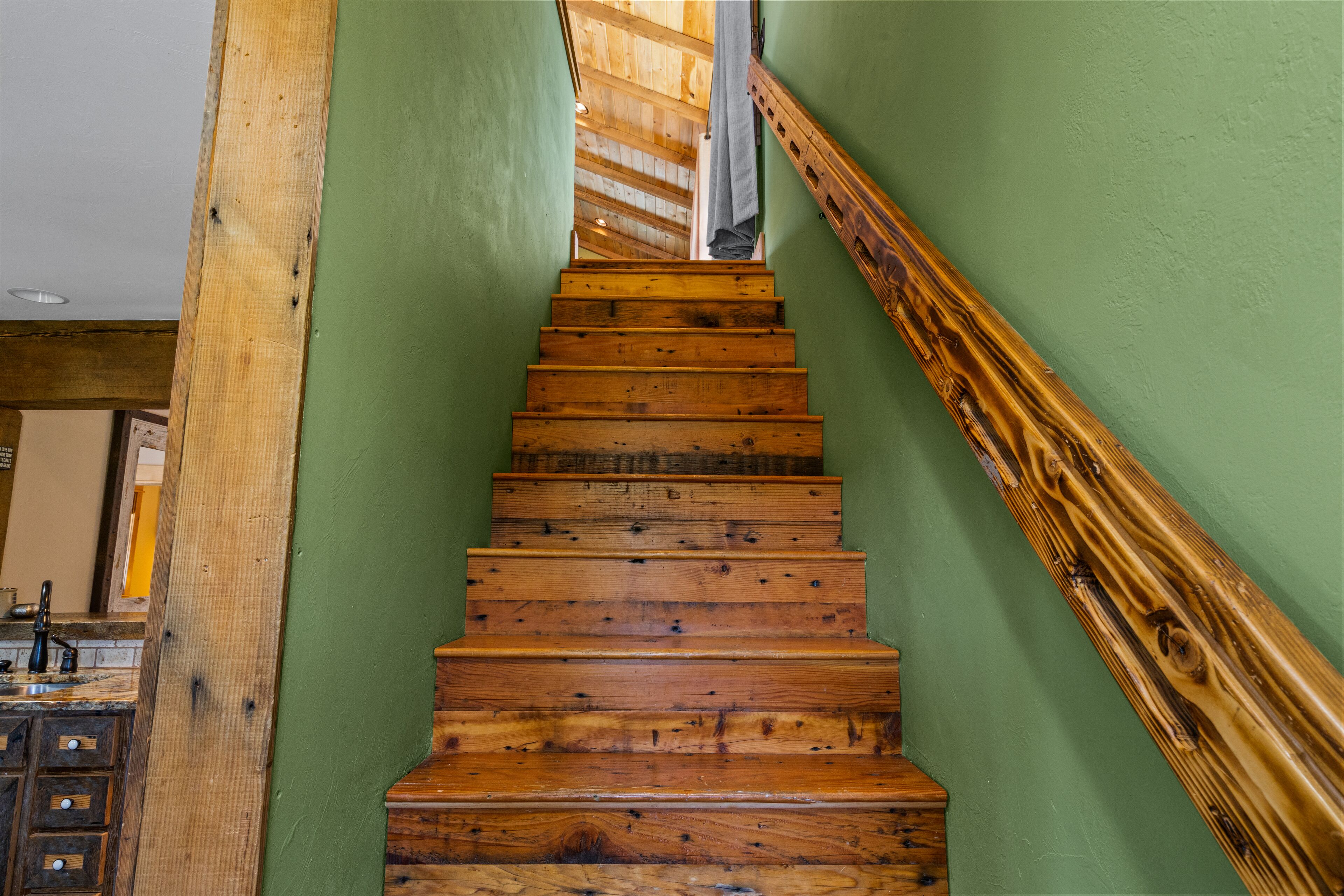 A wooden staircase with a green wall on one side and a wooden handrail on the other.