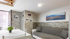 Ett rum med ett vitt bord, en grå soffa och en målning av en stadsbild på väggen.