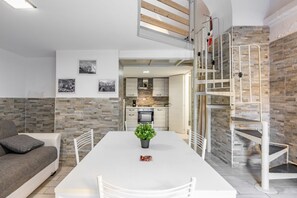 A modern living room with a white sofa, a dining table with a potted plant, and a kitchen in the background. - GuestHost - Functional Apt x5 in the Heart of Catania (Catania)