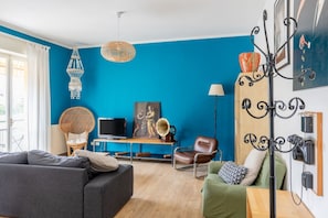 A living room with a blue wall, a sofa, a green armchair, a television, a decorative lamp, and a wall-mounted coat rack.