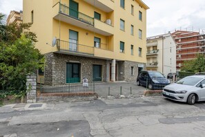 A multi-story building with a stone facade, balconies, and parked cars.