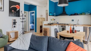 Une cuisine moderne aux murs bleus, un coin repas avec une table et des chaises, et un salon avec un canapé et une table basse.