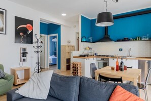 A modern kitchen with blue walls, a dining area with a table and chairs, and a living room with a sofa and a coffee table.