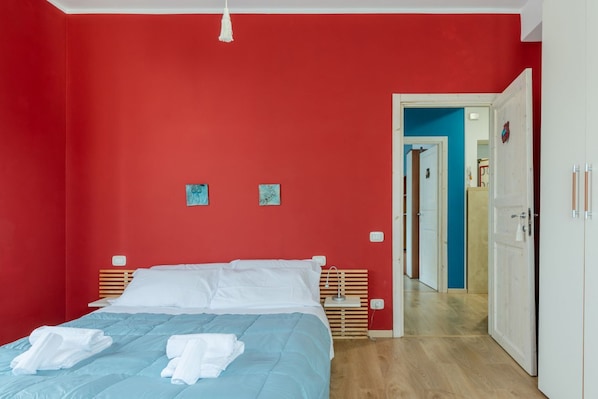 A room with a bed, a white door, and a hallway leading to another room.