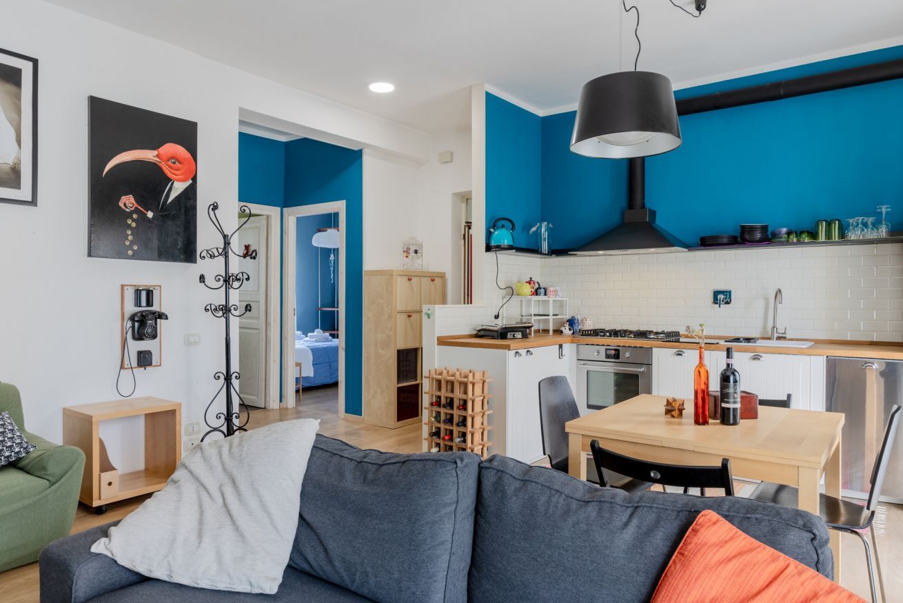 Een moderne keuken met blauwe wanden, een eethoek met tafel en stoelen, en een woonkamer met een bank en salontafel.
