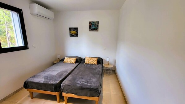 A room with two beds, a window, an air conditioner, and two wall-mounted pictures.