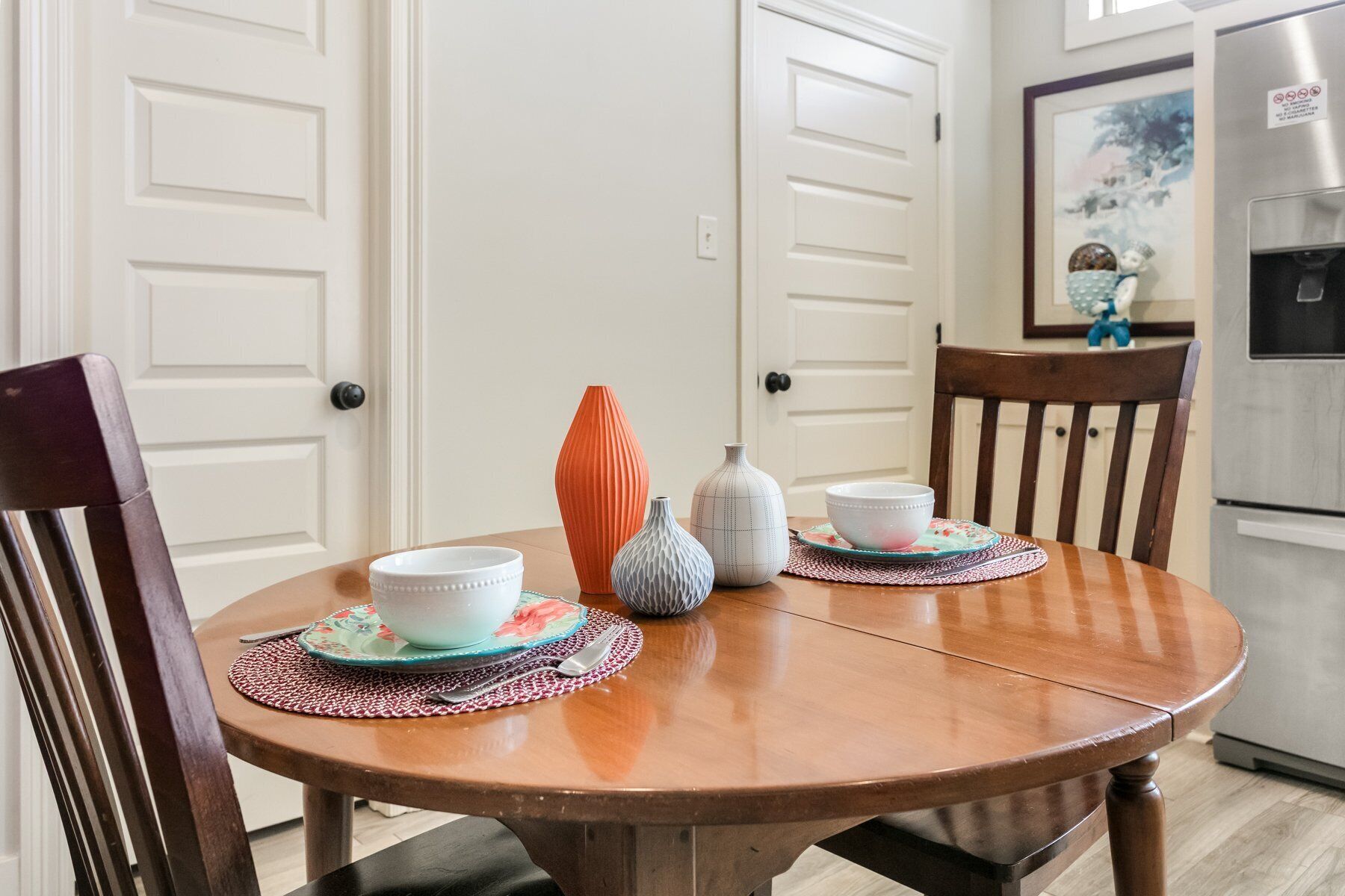 A dining table with four chairs, a white door, and a kitchen area with a refrigerator.