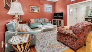 Un salon avec un canapé de couleur turquoise, un fauteuil à motifs floraux, une table basse en verre et un tapis à motifs.