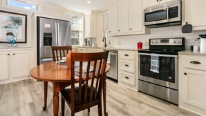 Une cuisine moderne avec des meubles blancs, des appareils en acier inoxydable et une table à manger en bois.