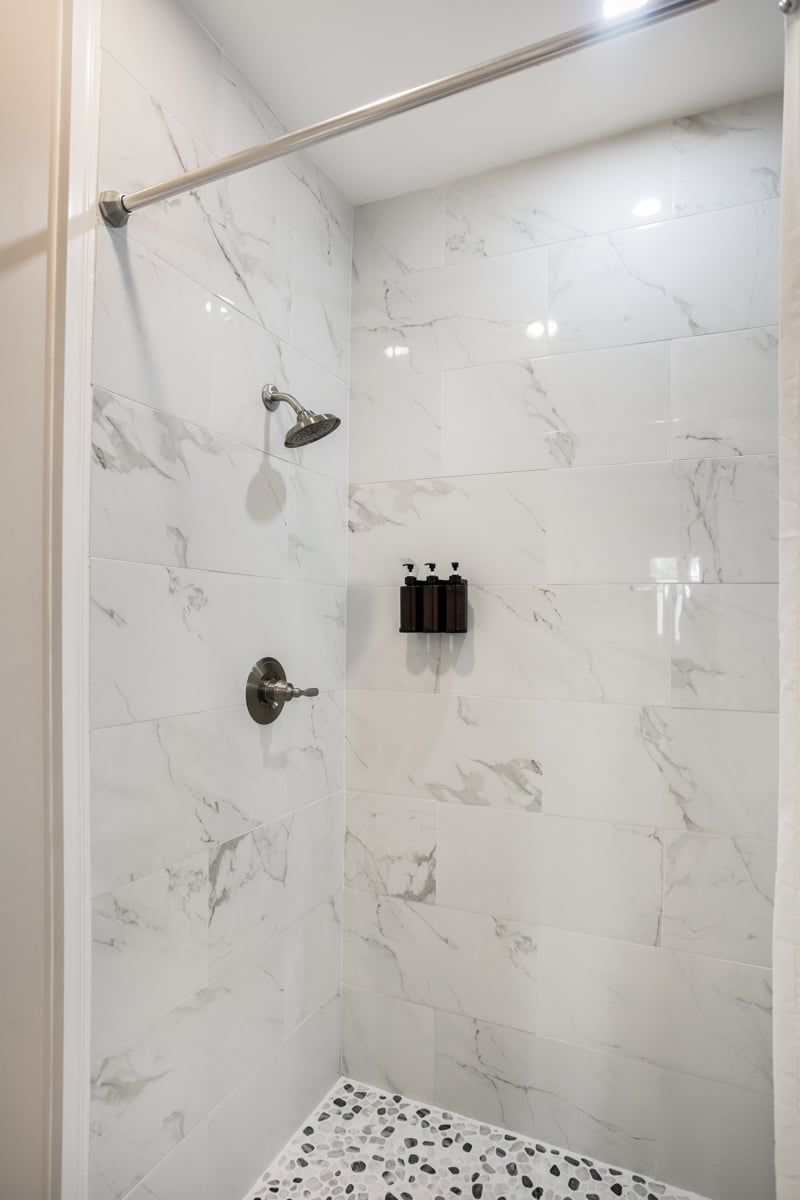 A shower with a marble wall, a handheld showerhead, and a handheld shower attachment.