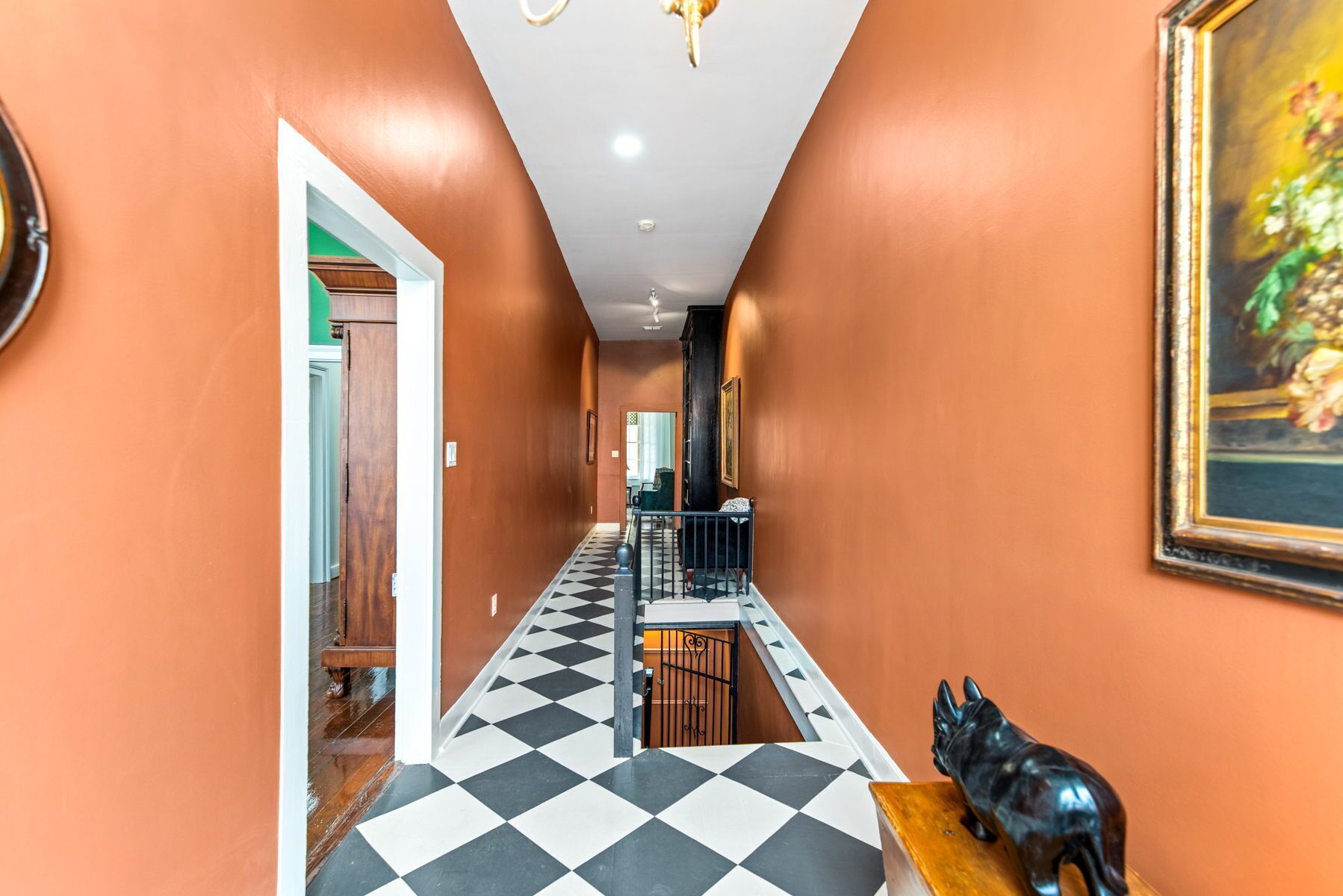A hallway with a checkered floor, a black statue, and a painting on the wall.