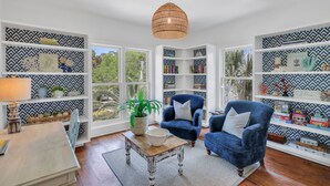 Un salon chaleureux avec une grande fenêtre, des étagères blanches à motifs, un fauteuil bleu et une table basse en bois.