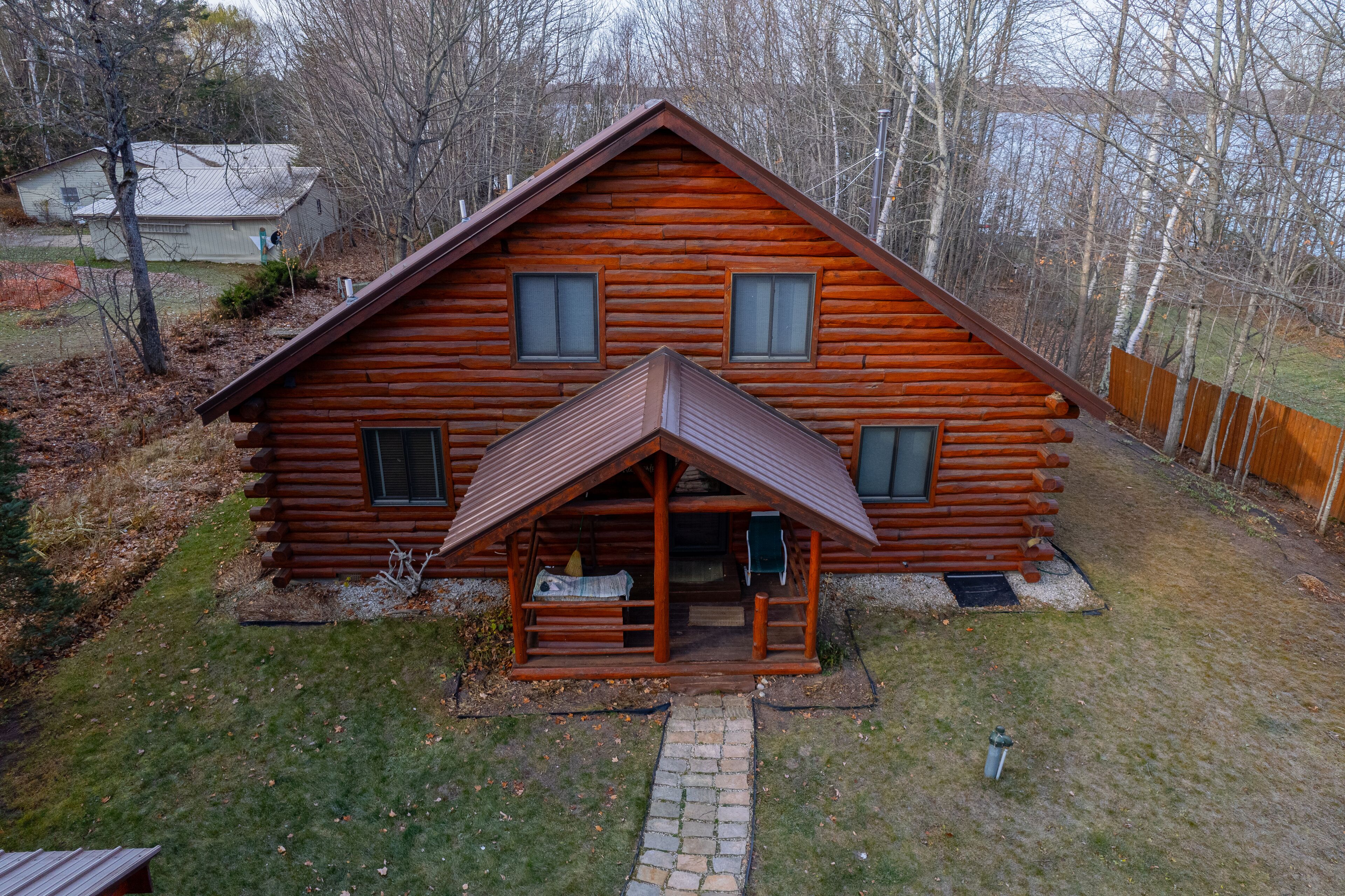 Une cabane en rondins avec un porche, une cheminée et un petit jardin devant.