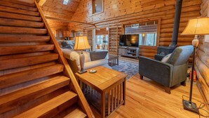 A log cabin interior with a wooden staircase, a sofa, a coffee table, a television, and a fireplace.