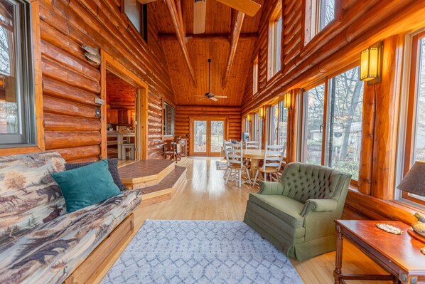 A log cabin interior with a dining area, a sofa with a moose print, and a green armchair.