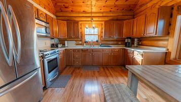 A wooden cabin kitchen with a refrigerator, stove, microwave, and wooden cabinets.