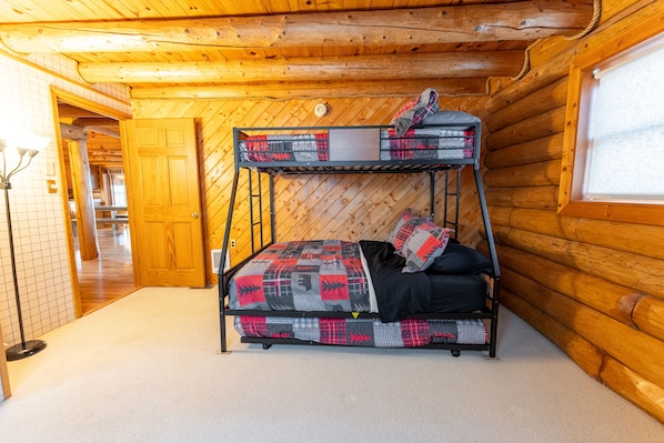 Una cama litera con una manta a cuadros y almohadas, techo de madera y ventana con vistas.