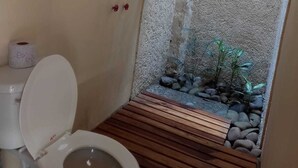 Un baño con inodoro, ducha y suelo de madera, además de un pequeño jardín de rocas.