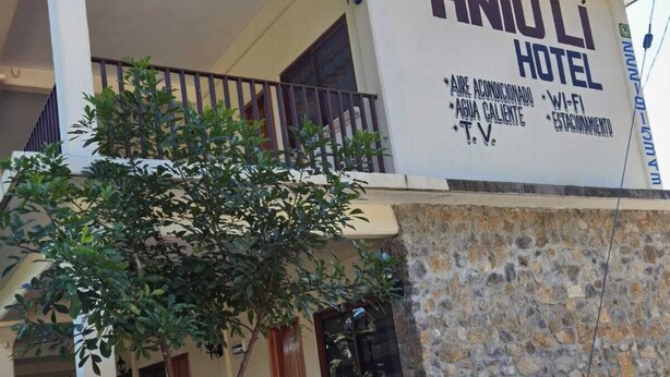 A two-story building with a sign reading "HNIÚ LI HOTEL" and amenities listed including air conditioning, hot water, Wi-Fi, TV, and parking.