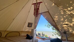 Une tente avec deux lits, une décoration en macramé suspendue et une vue sur la mer.