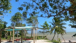 Une plage avec une structure en bois, un hamac et un espace ombragé.