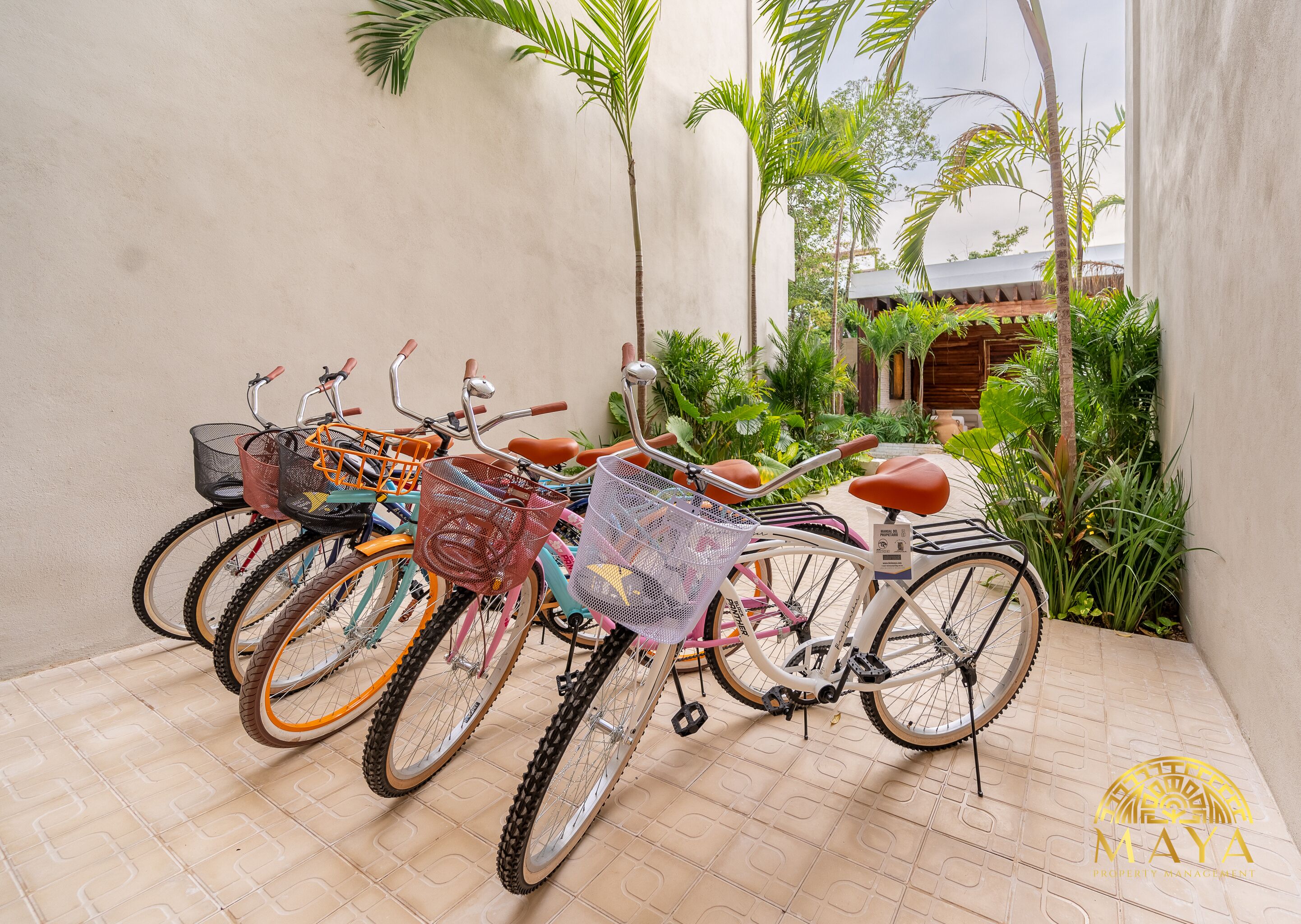 Bicicletas estacionadas en un área exterior con piso de baldosas, rodeadas de vegetación y un edificio al fondo.
